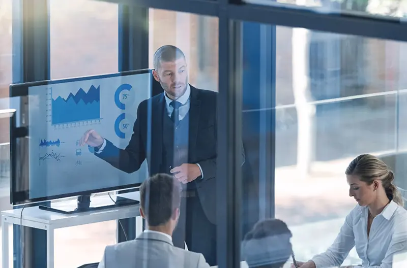 Financial team member outlining investment data on a monitor for the group to dissect and plan financial vehicles accordingly.